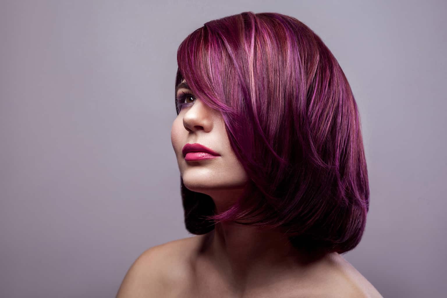 Portrait of beautiful fashion model woman with short purple colored hairstyle and makeup and looking away. indoor studio shot, isolated on gray background.